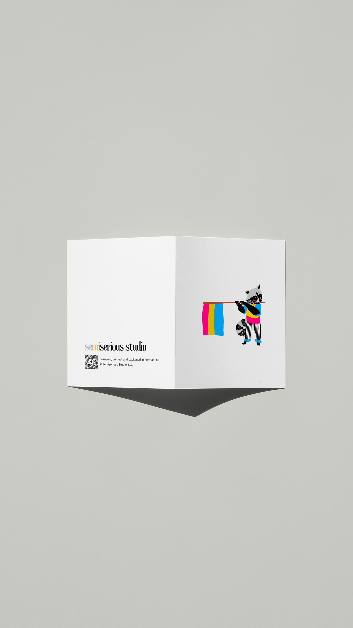 Raccoon Pansexual Pride card standing open, showing the front artwork and the Semiserious Studio logo on the back