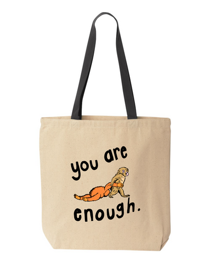 Natural canvas tote bag with black handles, printed with a small monkey holding an orange stuffed animal and the words you are enough