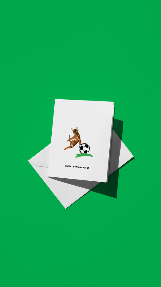 Hand-drawn illustration of an Abyssinian cat playing soccer with the message "HAPPY BIRTHDAY ARIES"