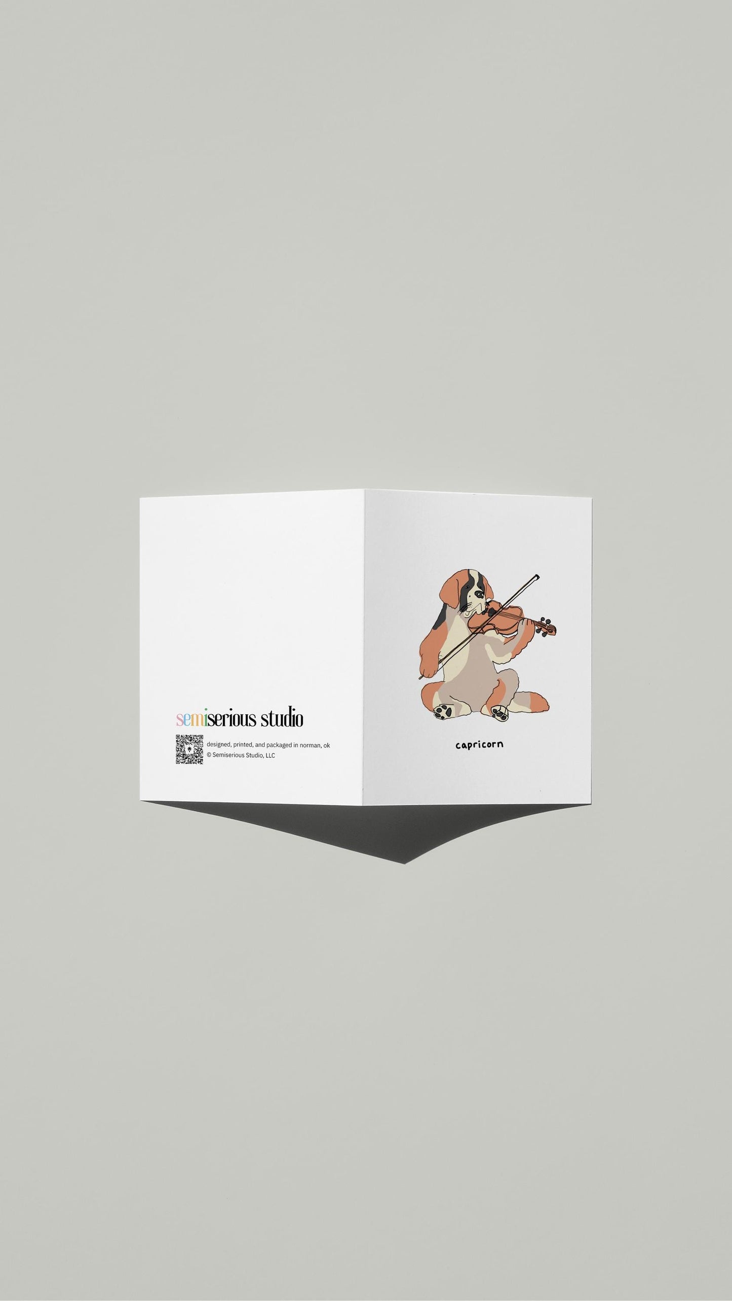Capricorn St. Bernard Violin Birthday card standing open, showing the front artwork and the Semiserious Studio logo on the