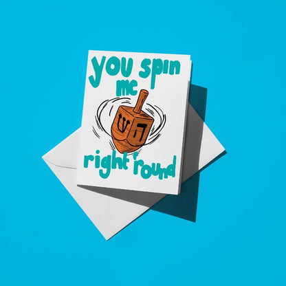 Wooden dreidel spinning, with teal text reading "you spin me right round"