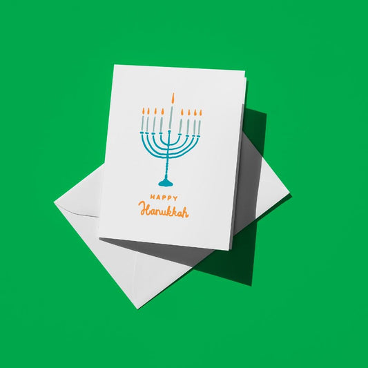 Blue menorah with lit candles above orange text reading "Happy Hanukkah"