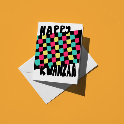 "Happy Kwanzaa" above a woven mkeka mat in pink, green, yellow and teal checks