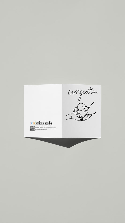 New Baby Congratulations card standing open, showing the front artwork and the Semiserious Studio logo on the back