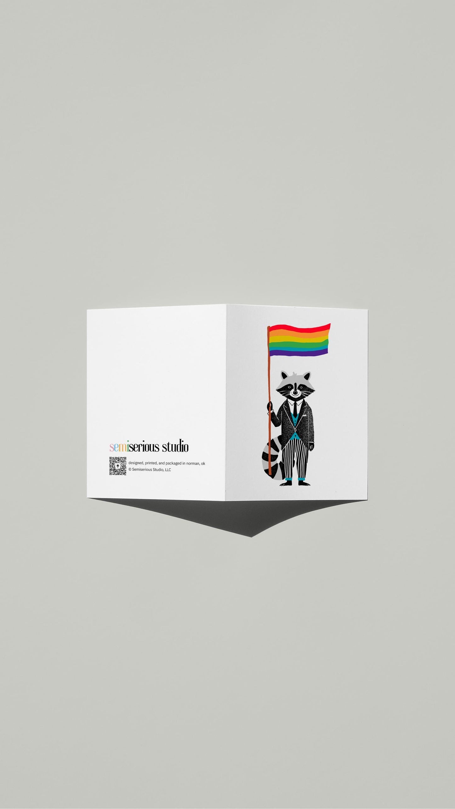 Raccoon Rainbow Pride card standing open, showing the front artwork and the Semiserious Studio logo on the back