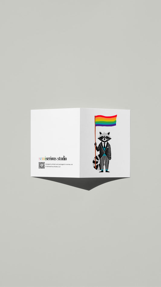 Raccoon Rainbow Pride card standing open, showing the front artwork and the Semiserious Studio logo on the back