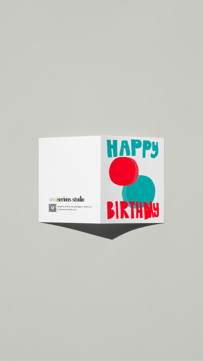 Red & Blue Balls Birthday card standing open, showing the front artwork and the Semiserious Studio logo on the back
