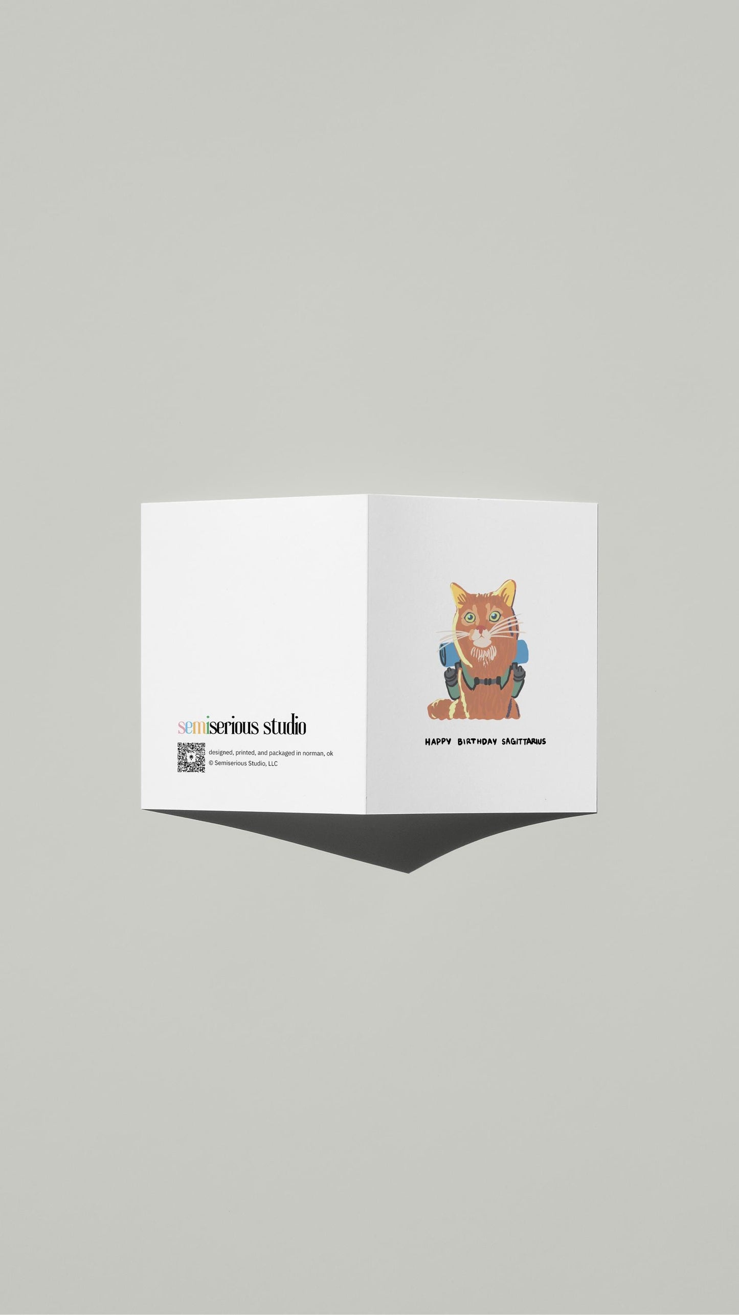 Sagittarius Cat Hiking Birthday card standing open, showing the front artwork and the Semiserious Studio logo on the back