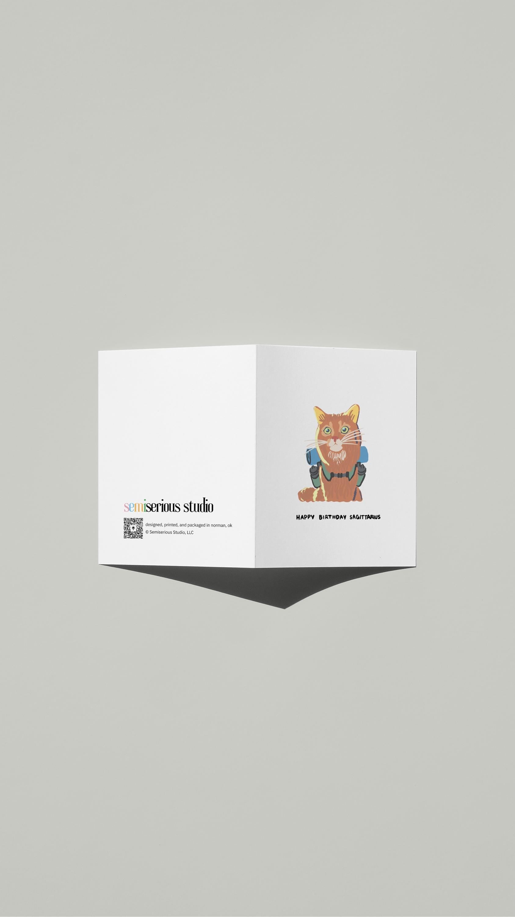 Sagittarius Cat Hiking Birthday card standing open, showing the front artwork and the Semiserious Studio logo on the back