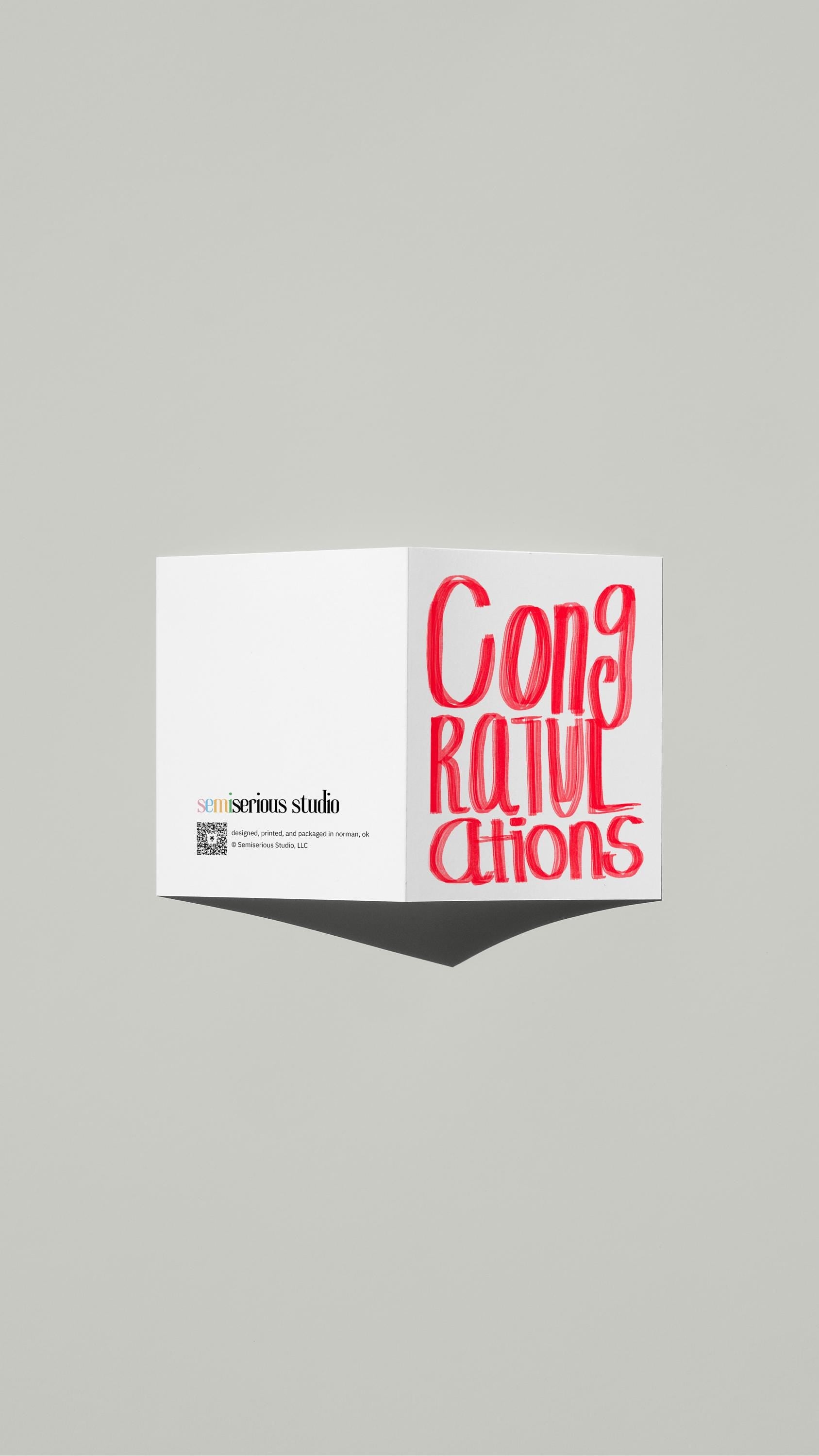 Simple Red Congratulations card standing open, showing the front artwork and the Semiserious Studio logo on the back