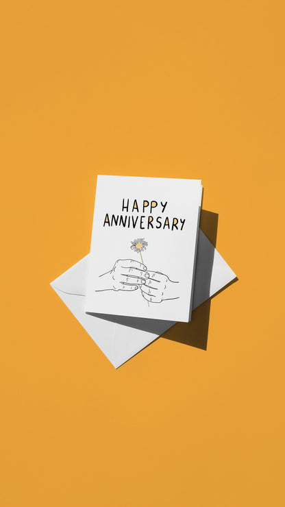 Hand-drawn illustration of hands holding a single small flower with the message "HAPPY ANNIVERSARY"
