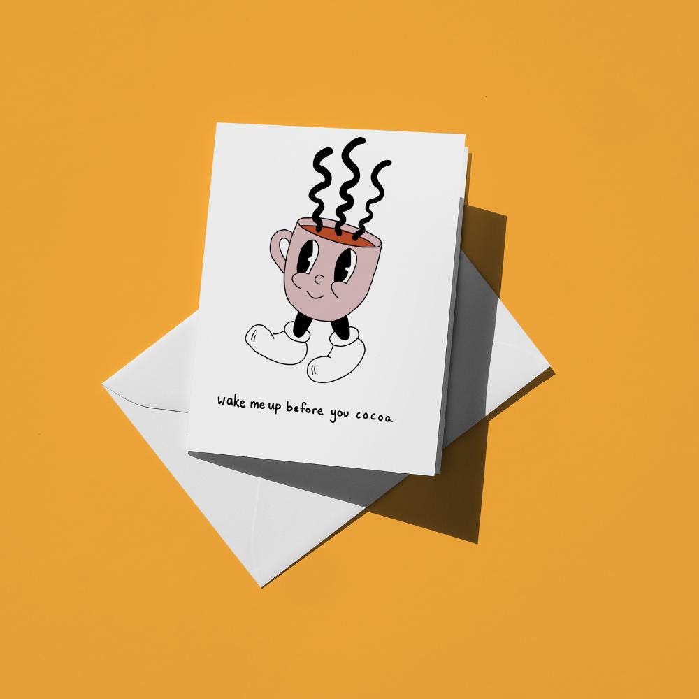 Steaming mug of cocoa with a face, reading "wake me up before you cocoa"